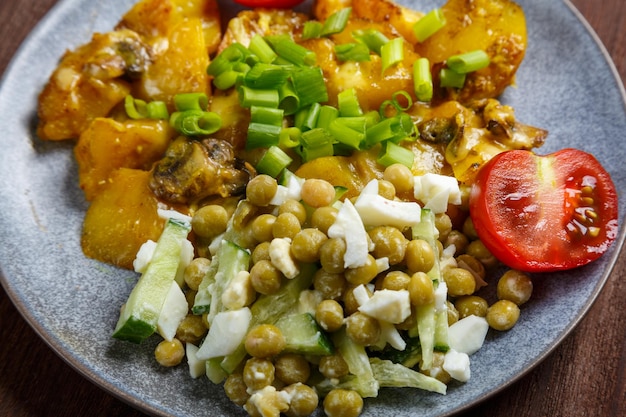 Pommes de terre au four avec du fromage et des côtes levées garnies de tomates cerises et de pois verts dans une assiette en gros plan