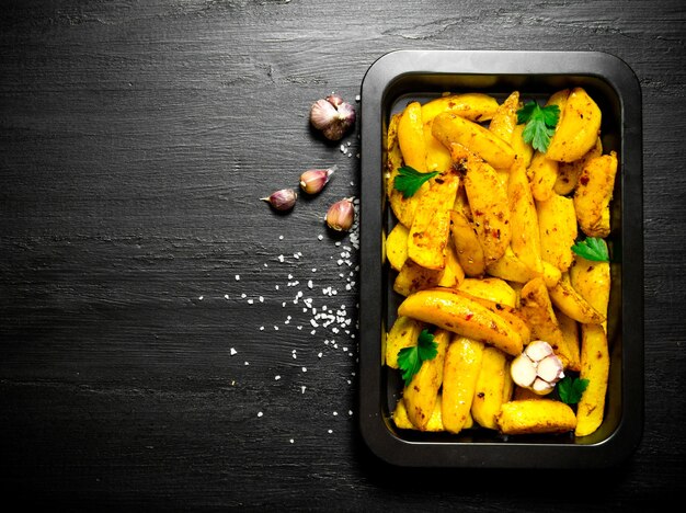 Pommes de terre au four avec des épices et du sel sur une table en bois noire.