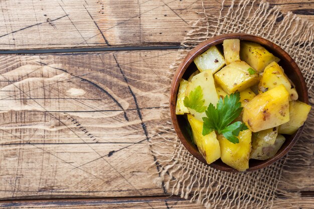 Pommes de terre au four avec des épices et des herbes dans une assiette en bois. Espace de copie