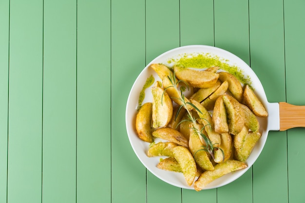 Pommes de terre au four avec sauce verte et romarin sur une plaque blanche sous la forme d'une poêle. Pommes de terre frites avec sauce pesto sur une table verte.