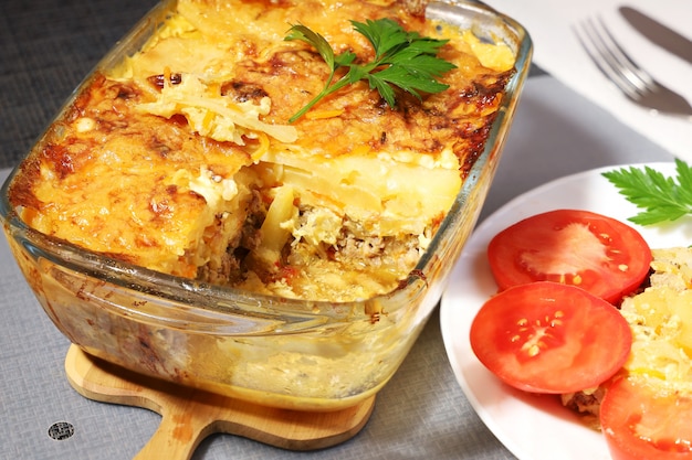 Pommes de terre au four avec de la viande dans un récipient en verre, portion en surbrillance près du plat avec des tomates