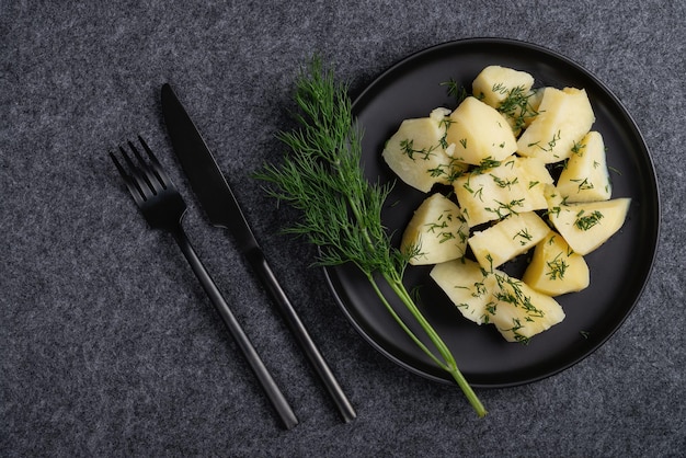 Pommes de terre bouillies et aneth sur une plaque noire sur fond sombre