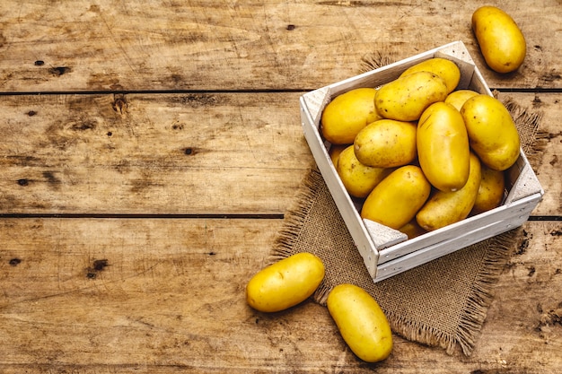 Pommes de terre crues entières non pelées dans une caisse en bois. Nouvelle récolte, sur un sac, fond de planches de bois