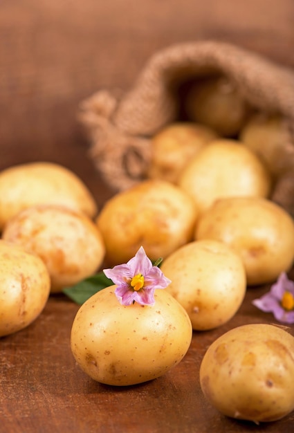 Pommes de terre crues avec des fleurs dans le sac sur le fond en bois