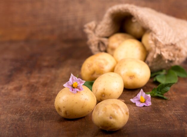 Pommes de terre crues avec des fleurs dans le sac sur le fond en bois