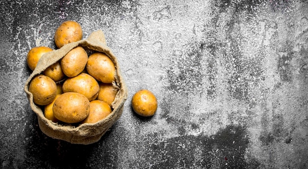 Pommes de terre dans un vieux sac sur fond rustique