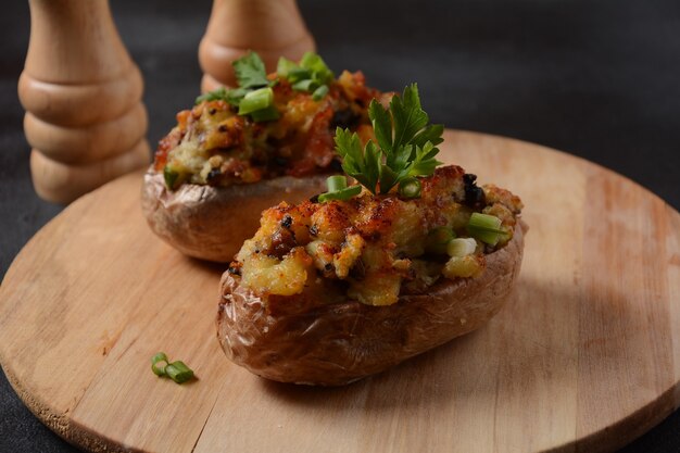 Pommes de terre farcies au four avec bacon, oignon vert, champignons et fromage sur une planche en bois. Style rustique