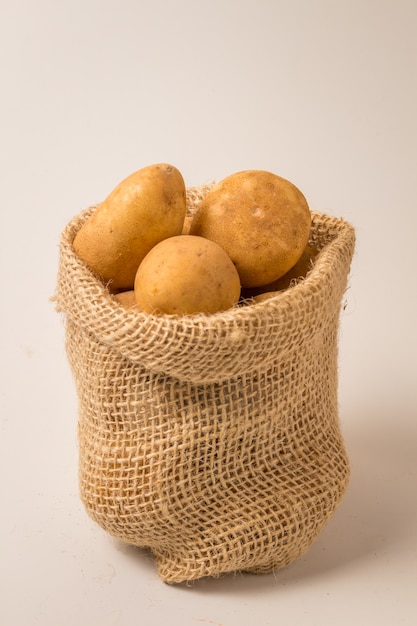 Pommes de terre fraîches et crues dans un sac rustique isolé sur blanc