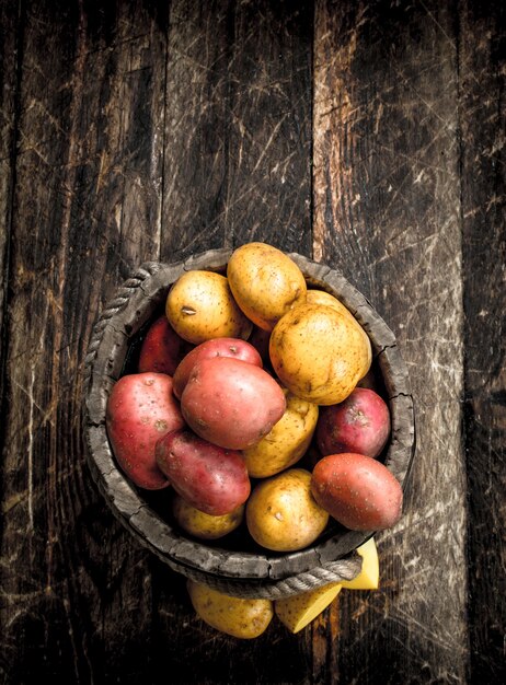 Photo pommes de terre fraîches dans un seau en bois. sur un fond en bois.