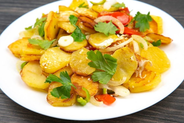 Pommes de terre frites aux herbes et légumes dans une assiette blanche sur une table en bois