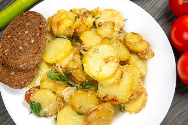 Pommes de terre frites cuites aux herbes et légumes dans une assiette blanche sur une table en bois