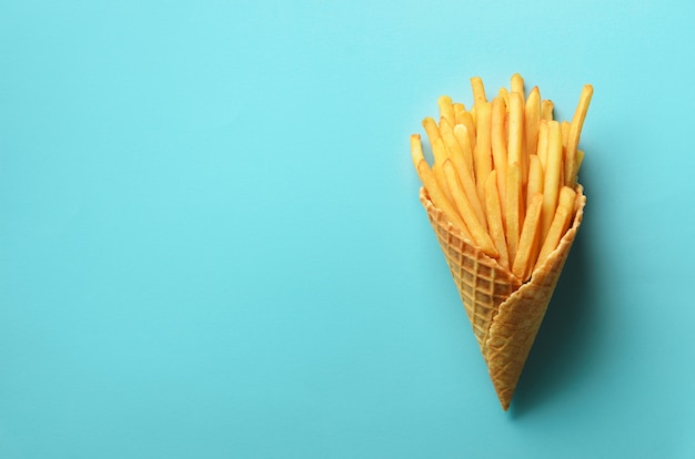 Pommes de terre frites dans des cônes de gaufres sur fond bleu. Frites salées chaudes avec sauce tomate, feuilles de basilic. Restauration rapide, malbouffe, concept de régime.