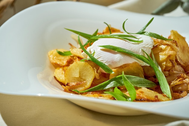 Pommes de terre frites avec un œuf poché dans une assiette sur une nappe blanche