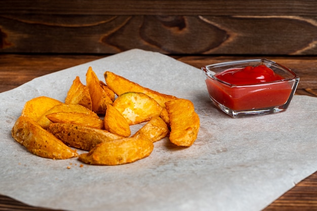 Pommes de terre frites rustiques sur un fond de papier avec du ketchup.