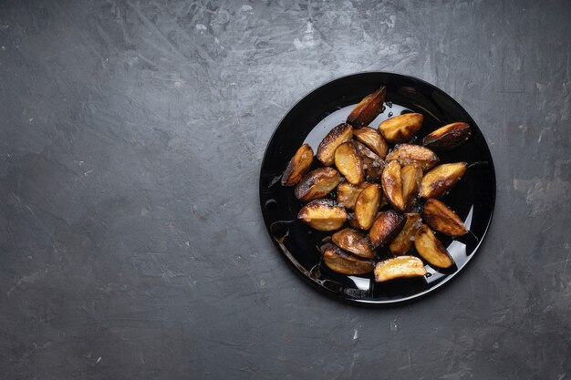 Pommes de terre frites rustiques sur un plat noir sur la table, vue de dessus