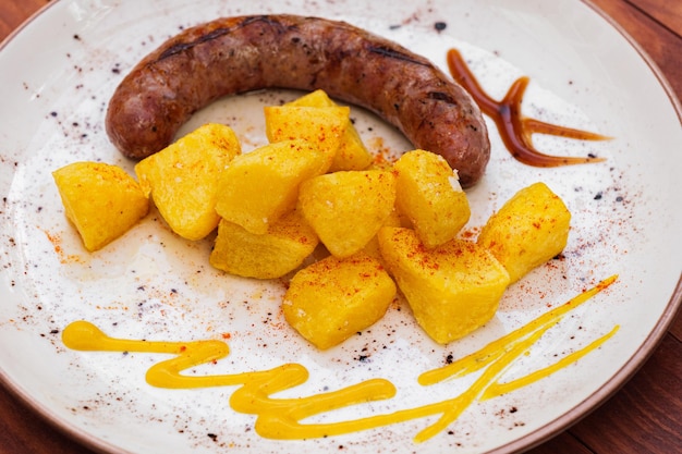 Pommes de terre frites et saucisse de porc espagnole traditionnelle butifarra avec sauces sur plaque blanche