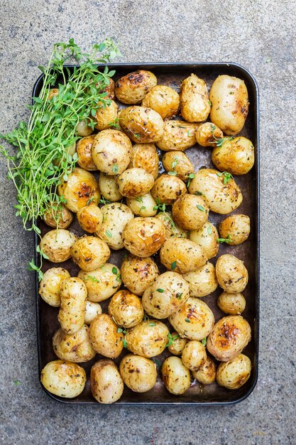 Pommes de terre grelots entières rôties avec légumes verts et huile d'ail sur pierre grise