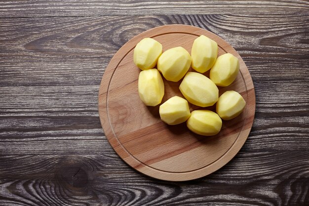 Pommes de terre pelées sur une planche à découper en bois sur table marron