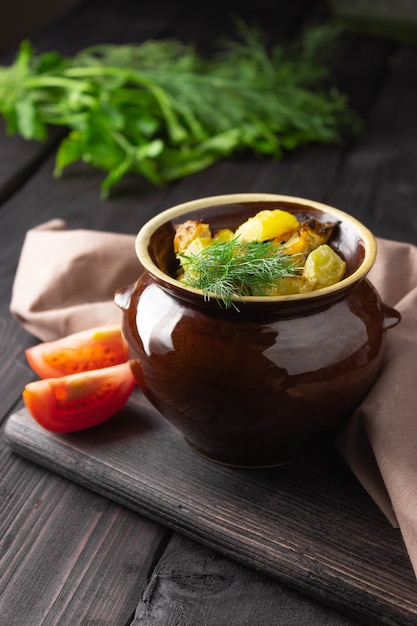 Pommes de terre, poulet et courgettes cuits dans un pot en argile sur fond sombre.