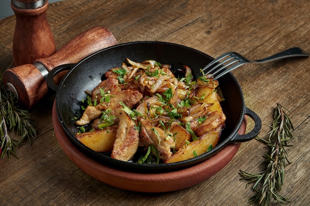 Pommes de terre sautées au bacon, oignons et herbes dans une poêle décorative sur une surface en bois. Gros plan, mise au point sélective.