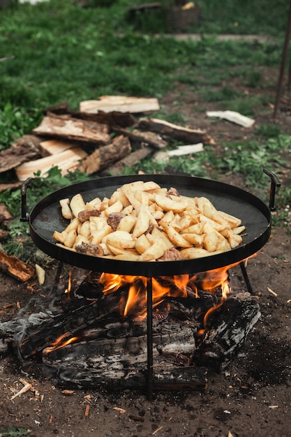 Les pommes de terre sont frites sur le bûcher. La nature au village. Le processus de cuisson des aliments. Journaux en arrière-plan.