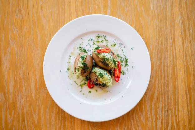 Pommes de terre en veste décorées de poivron rouge et d'herbes sur une assiette blanche