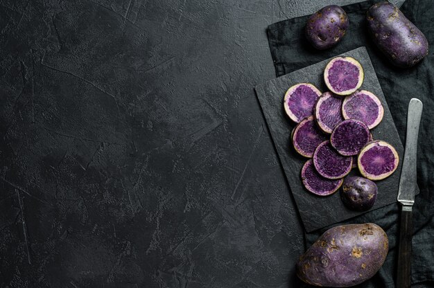 Pommes de terre violettes tranchées crues. Fond noir. Vue de dessus. Espace pour le texte