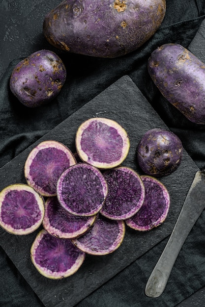 Pommes de terre violettes tranchées crues. Fond noir. Vue de dessus