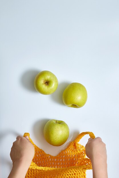 Les pommes tombent dans un sac de ficelle en filet jaune ouvert. mains féminines dans le cadre.