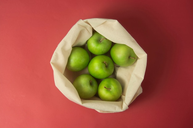 Pommes vertes dans un sac fourre-tout sur fond rouge. Concept zéro déchet.