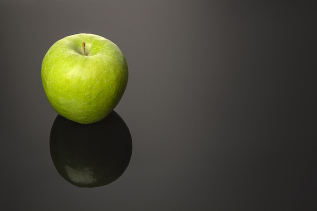 Pommes vertes avec des gouttes d'eau sur une table réfléchissante, isolée sur fond sombre. Copiez l'espace. Surface du miroir.