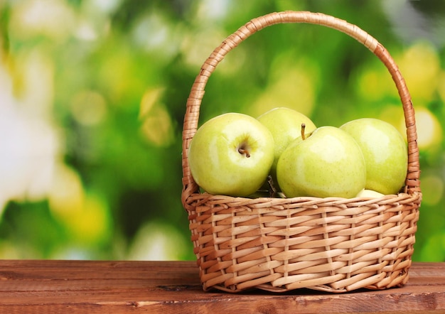 Pommes vertes juteuses dans le panier sur une table en bois sur fond vert