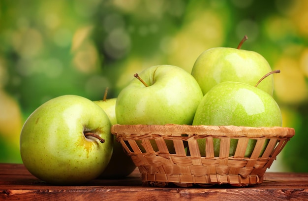 Pommes vertes juteuses dans le panier sur une table en bois sur fond vert