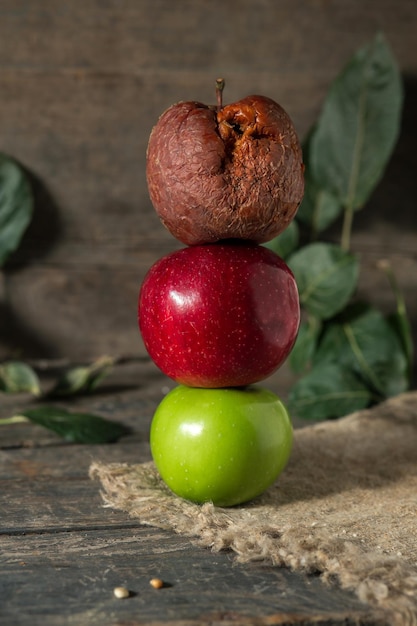 Pommes vertes rouges et pourries sur toile de jute sur planches de bois