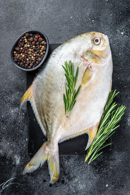 Pompano de poisson cru aux herbes sur une planche de marbre. Fond noir. Vue de dessus.