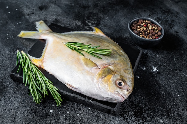 Pompano de poisson cru aux herbes sur une planche de marbre. Table noire. Vue de dessus.