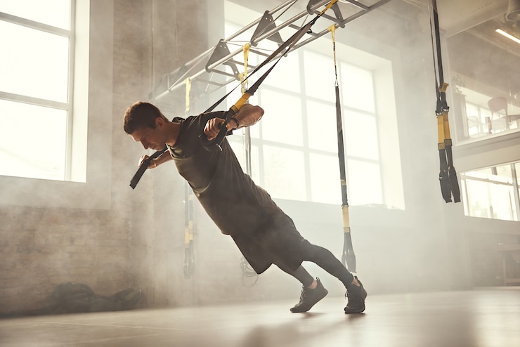 Photo pompe parfaite. vue latérale d'un homme athlétique jeune et fort en vêtements de sport faisant des pompes avec des sangles de fitness trx au gymnase