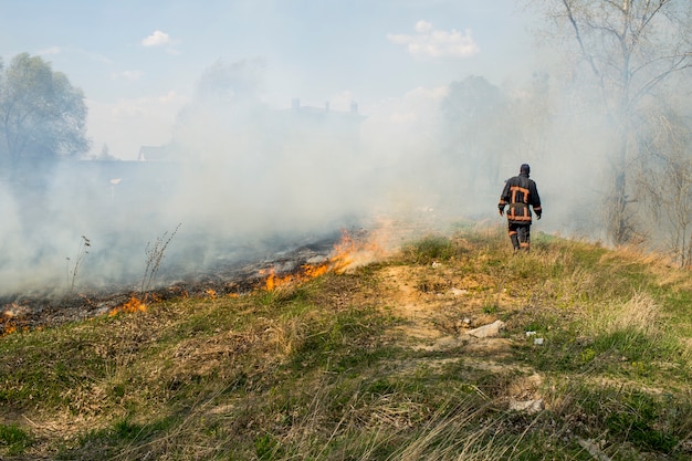 Pompier en arrière-plan d'un incendie, feu de forêt brûlant dans l'herbe de printemps et les brindilles
