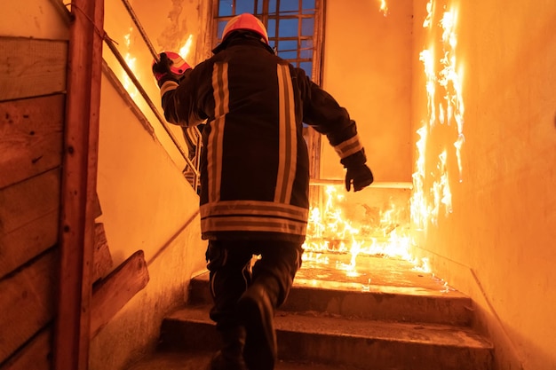 Un pompier courageux monte à l'étage pour sauver et secourir des personnes dans un immeuble en feu. Ouvrez le feu et la flamme. Low light hi est une photo de stock de mise au point sélective.