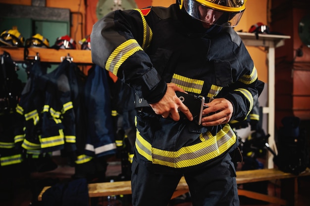 Pompier portant un uniforme de protection et se préparant à l'action en se tenant debout dans la caserne des pompiers.