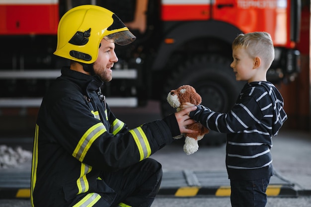 Un pompier prend un petit enfant garçon pour le sauver Voiture de pompier sur fond Pompier avec enfant dans ses bras Concept de protection