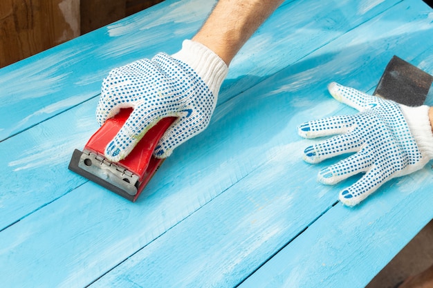 Ponçage avec des abrasifs dans une table en bois bleu peint en bois à la main