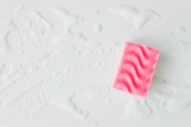 Éponge rose avec mousse détergente sur fond blanc gros plan Concept de nettoyage