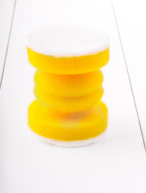 Éponges jaunes pour laver la vaisselle sur fond en bois blanc
