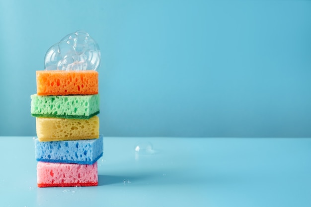 Éponges de nettoyage colorées avec des bulles de savon sur le mur bleu