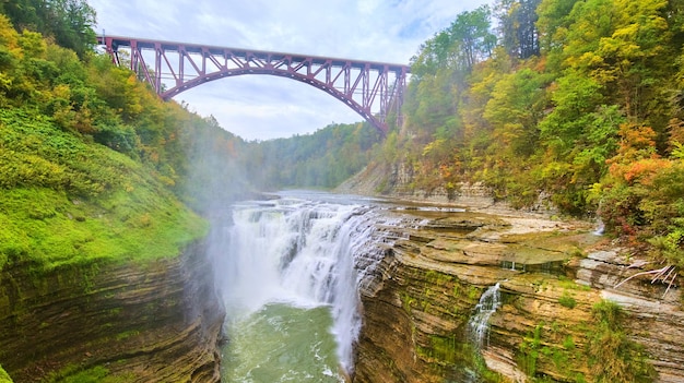 Pont en acier marron au-dessus d'une superbe cascade déchaînée coupant à travers des falaises en couches dans un écrin de verdure