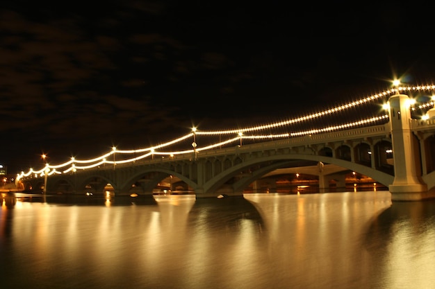 Photo pont éclairé sur la rivière contre le ciel la nuit