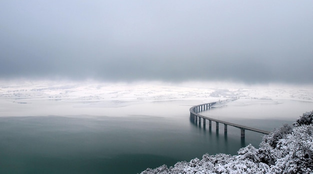 Un pont un jour brumeux avec quelques montagnes enneigées en arrière-plan.