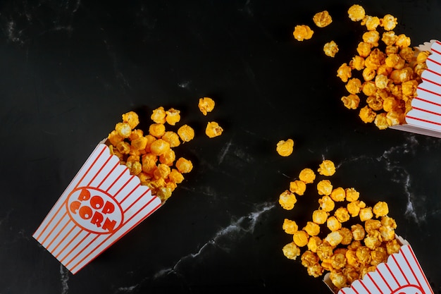 Pop-corn dans des boîtes rayées renversé sur une surface noire