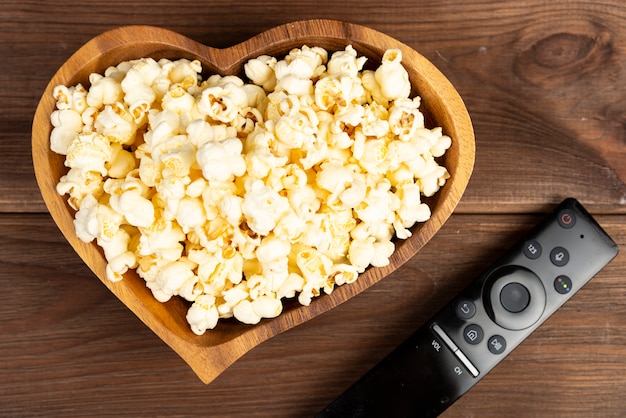 Pop-corn en forme de coeur dans un bol en bois et télécommande de télévision sur une table en bois